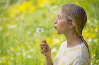 Porträt eines Teenagers, der auf einer Blumenwiese einen Pusteball bläst - WWF003311