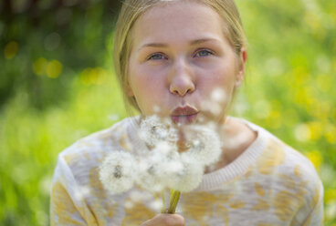 Portrait of teenage girl blowing blowballs on a flower meadow - WWF003312