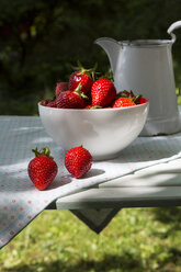 Schale mit Erdbeeren und Glas auf einem Tuch im Garten - LVF001247