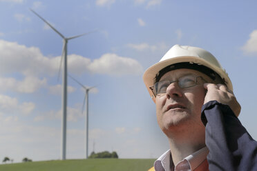 Germany, technician with safety helmet in front of wind turbines - SGF000680