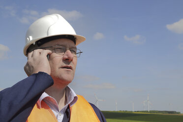 Germany, technician with safety helmet in front of wind turbines - SGF000681