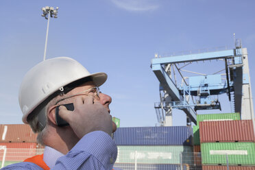 Porträt eines Mannes, der mit einem Smartphone vor einem Frachtcontainer telefoniert - SGF000688