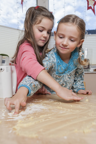Porträt von zwei kleinen Mädchen mit Teigresten auf dem Küchentisch, lizenzfreies Stockfoto