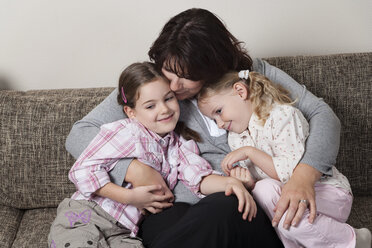 Mutter, die ihre beiden Töchter auf der Couch umarmt - ECF000638