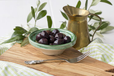 Schale mit schwarzen Oliven und Gabel auf einem Brett aus Olivenholz - YFF000135