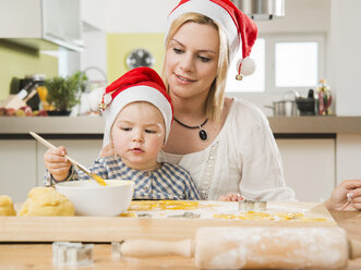 Mother and daughter wearing Santa hats baking in kitchen - UUF000509