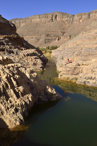 Afrika, Algerien, Tassili N'Ajjer National Park, Iherir, Frau ruht sich in der Nähe von Wasser in einem Guelta aus, Idaran Canyon, lizenzfreies Stockfoto