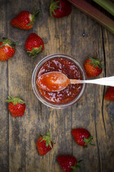 Glass of strawberry rhubarb jam, strawberries and rhubarb on dark wood, view from above - LVF001257