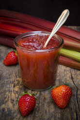 Glass of strawberry rhubarb jam, strawberries and rhubarb on dark wood - LVF001259