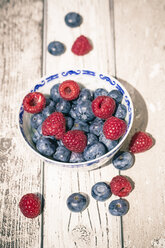 Schale mit Blaubeeren und Himbeeren auf weißem Holztisch, Blick von oben - SARF000614