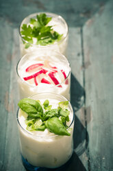 Three garnished glasses of curd with herbs on wooden tray, elevated view - SARF000604