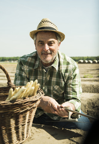 Germany, Hesse, Lampertheim, portrait of senior farmer cutting asparagus, Asparagus officinalis stock photo