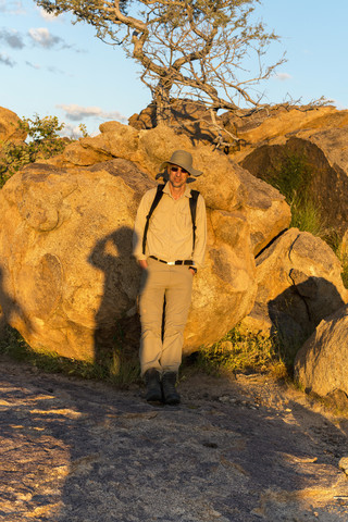 Afrika, Namibia, Erongo-Gebirge, Wanderer steht vor einem Felsen bei Sonnenuntergang, lizenzfreies Stockfoto