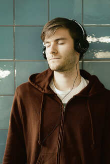 Junger Mann mit Kopfhörern, der an einer gekachelten Wand lehnt - MEMF000312