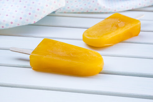 Two mango apple ice cream lollies and cloth on white wood - LVF001276