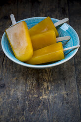 Bowl of four mango apple ice cream lollies on dark wood - LVF001279