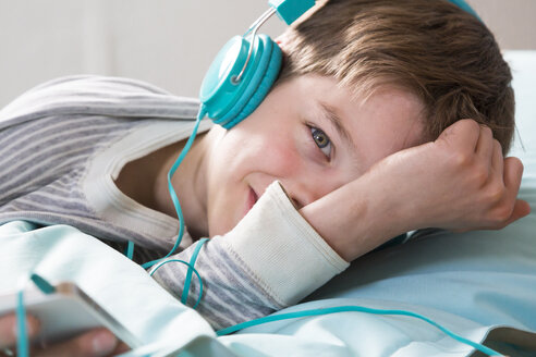 Porträt eines lächelnden Jungen mit Kopfhörern, der auf einem Sitzsack liegt - LVF001283