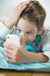 Porträt eines Jungen mit Smartphone und Kopfhörern auf einem Sitzsack liegend - LVF001285