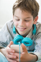 Porträt eines lächelnden Jungen mit Smartphone und Kopfhörern auf einem Sitzsack liegend - LVF001286