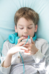 Portrait of boy with smartphone and headphones lying on beanbag - LVF001287