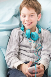 Porträt eines lächelnden Jungen mit Smartphone und Kopfhörern auf einem Sitzsack liegend - LVF001288