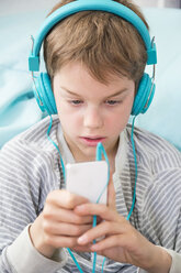 Portrait of boy with smartphone and headphones lying on beanbag - LVF001289