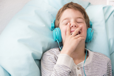 Porträt eines lachenden Jungen, der mit Kopfhörern auf einem Sitzsack liegend Musik hört, lizenzfreies Stockfoto