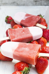 Three strawberry ice cream lollies and strawberries on white wood - LVF001282