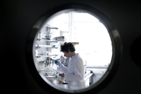 Female chemist working in lab watched through spy hole - SGF000708