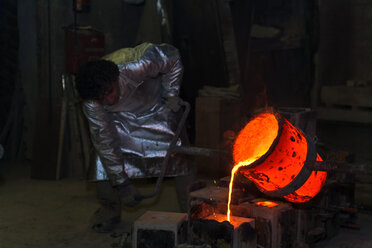 Deutschland, München, Gießereiarbeiter gießt heißes Metall in Gussform - TCF004029