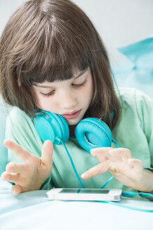 Porträt eines kleinen Mädchens mit Kopfhörern und Smartphone - LVF001313