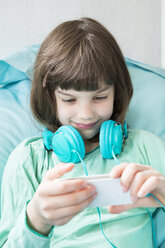 Porträt eines kleinen Mädchens mit Kopfhörern und Smartphone - LVF001315