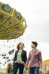 Teenage couple at fun fair with chairoplane in the background - UUF000640