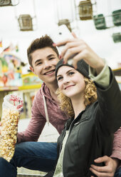 Teenager-Paar mit Popcorn, das sich auf dem Jahrmarkt fotografiert - UUF000632