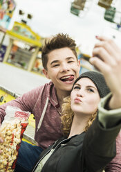 Porträt eines jugendlichen Paares mit Popcorn, das sich auf einem Jahrmarkt selbst fotografiert - UUF000630