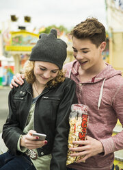 Portrait of happy teenage couple with popcorn looking at smartphone - UUF000628