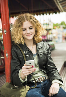 Porträt eines Teenagers, der auf einem Jahrmarkt sein Smartphone benutzt - UUF000652