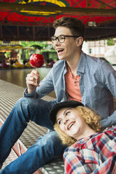 Portrait of happy teenage couple with candied apple at fun fair - UUF000670