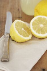 Geschnittene Zitrone, Messer, Tuch und Glas mit Zitronensaft auf Holz - SABF000029