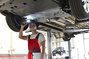 Car mechanic in a workshop checking underbody of a car - LYF000032