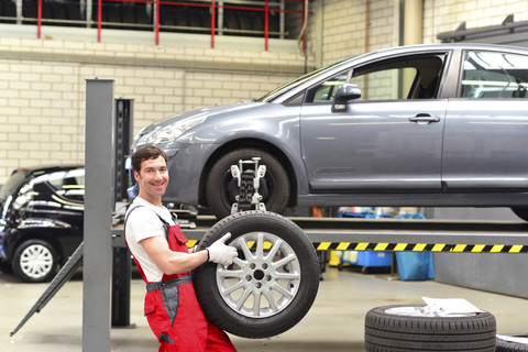 Porträt eines selbstbewussten Automechanikers in einer Werkstatt, der einen Reifen hält, lizenzfreies Stockfoto