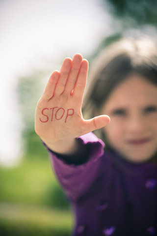 Kleines Mädchen zeigt Handfläche mit dem Wort STOPP darauf, lizenzfreies Stockfoto