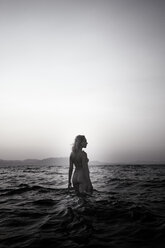 Nackte junge Frau beim Spaziergang im Meer in der Dämmerung - AJF000037