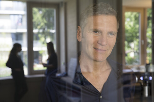 Portrait of smiling business man behind glass pane - FKF000492