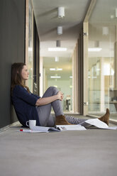 Porträt einer Geschäftsfrau, die im Flur eines Büros auf dem Boden sitzt - FKF000503