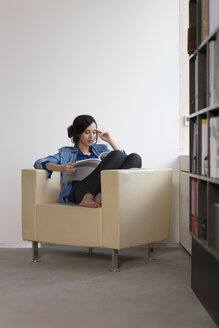 Porträt einer Geschäftsfrau, die auf einem Sessel sitzt und eine Zeitschrift liest - FKF000505