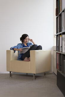 Portrait of business woman sitting on armchair reading magazine - FKF000505