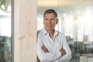 Portrait of smiling creative business man with crossed arms in front of glass pane - FKF000532
