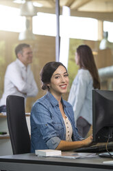 Porträt einer Geschäftsfrau am Schreibtisch mit kommunizierenden Kollegen im Hintergrund - FKF000542