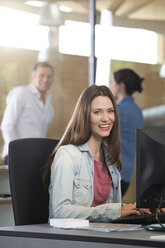 Porträt einer Geschäftsfrau am Schreibtisch mit kommunizierenden Kollegen im Hintergrund - FKF000543